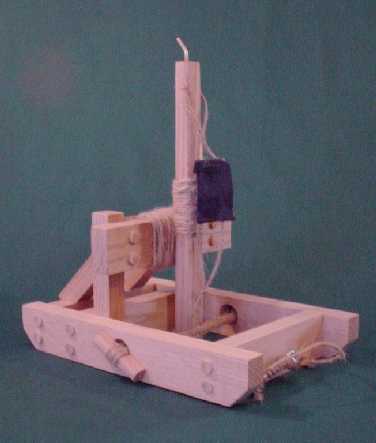Rear side view of a torsion catapult in the fired position showing the torsion bundle, arm, release pin, sling, and trigger mechanism.