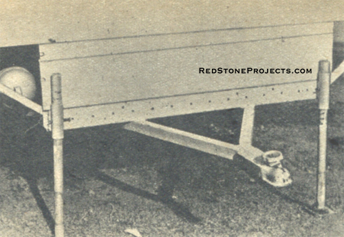 Closeup showing hitch and two of the four pipe stands that support the trailer when stops are made. One end of the bottled gas tank appears on the left.