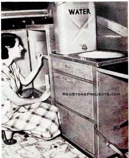 Woman demostrating the refridgerator in a vintage DIY camping trailer.