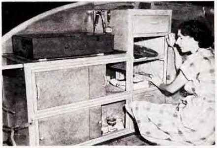 Woman showing the ample space in the kitchen cabinets of a vintage Kamp Master camper trailer.