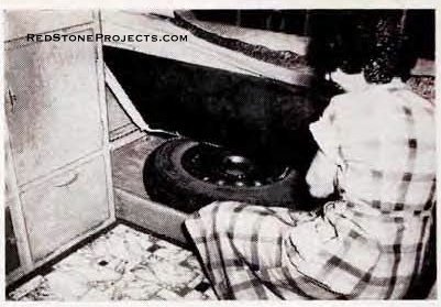 Woman showing the storage space beneath the studio couch in a vintage Wild Goose camper trailer.